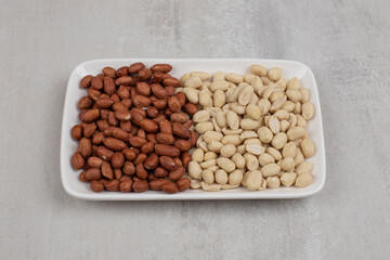Pile of peeled and unpeeled peanuts on white plate
