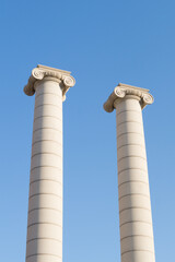 Two columns of the famous "Cuatro Columnas" or "Quatre columnes" of Barcelona (Catalonia, Spain). Two white columns or pillars with the blue sky in the background.