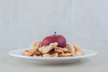 A white plate full of dried apple fruit with a whole apple