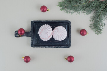 A dark wooden board with vanilla and pink zephyrs with Christmas balls