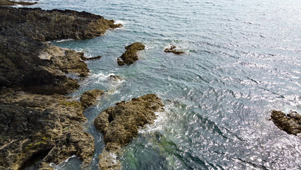 Wild rocky coast of the Atlantic Ocean. Small ripples and sun glare on the surface of the water. Seaside landscape on a sunny day.