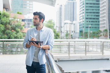 Young man using laptop computer working and video conference meeting at outdoor. Young creative man looking at screen typing message with tablet.Handsome young man using digital tablet