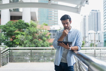 Young man using laptop computer working and video conference meeting at outdoor. Young creative man looking at screen typing message with tablet.Handsome young man using digital tablet
