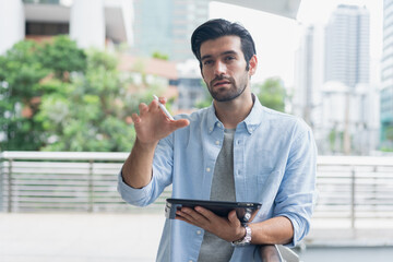 Young man using laptop computer working and video conference meeting at outdoor. Young creative man looking at screen typing message with tablet.Handsome young man using digital tablet