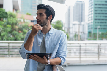 Young man using laptop computer working and video conference meeting at outdoor. Young creative man looking at screen typing message with tablet.Handsome young man using digital tablet