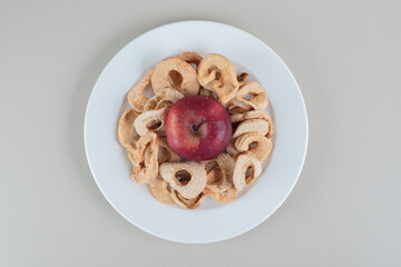 A white plate full of dried apple fruit with a whole apple