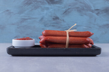 Smoked sausages and ketchup on dark plate