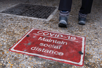 Red poster advising to keep distance due to Covid-19 contamination on a street in Cambridge, UK.
A pedestrian walks away from it. Focus on the word 'social'