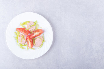 Plate of sliced sausages and tomatoes on stone background