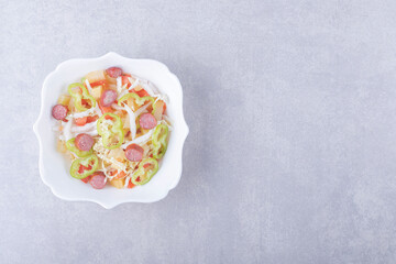 Bowl of smoked sausages and chopped vegetables on stone background