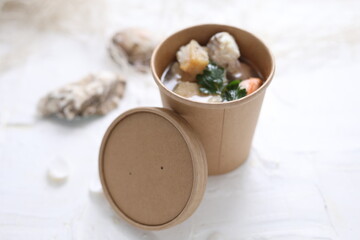Fish soup with salmon and shrimps. Fish broth soup in a take-away box, on a white background, top...