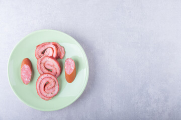 Ham rolls and smoked sausages on green plate