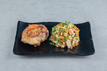 A black plate of chicken fried meat and vegetable salad