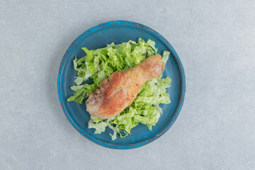 A wooden plate of fried chicken leg meat with sliced lettuce