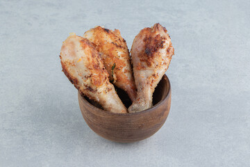 A wooden bowl full of baked chicken legs meat