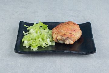 A black plate with fried chicken leg and lettuce salad