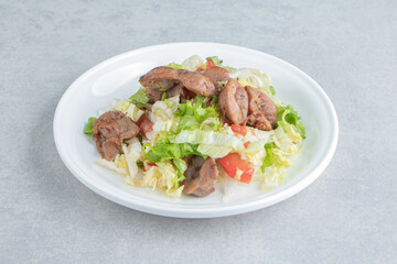 A white plate of fried meat and vegetable salad