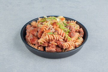 A black plate with spiral pasta with herbs