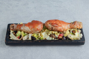 A wooden board with fried chicken legs with vegetable salad