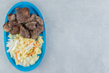 A blue wooden plate of fried meat and vegetable salad