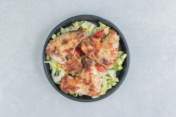A black bowl with fried chicken legs and vegetable salad