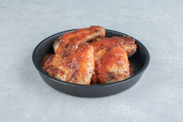 A black plate of fried meat in tomato sauce