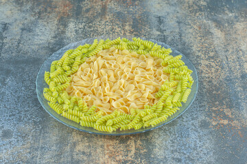 Bow tie and fusilli pasta in the bowl, on the marble background