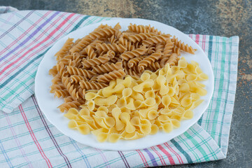 Brown fusilli pasta and farfalle pastas in the bowl on the towel, on the marble background