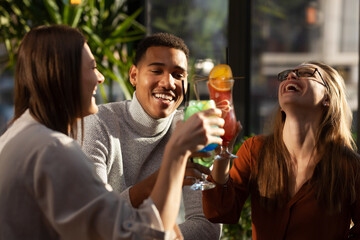 Three multiracial friends in a bar cheering. After work party with cocktails after successful work...