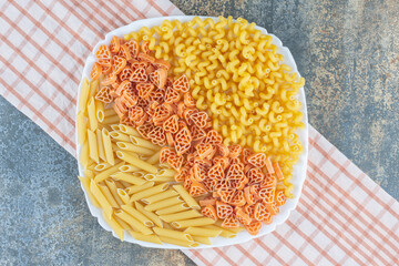 Heart shaped, penne and fusilli pastas in bowl on towel, on the marble background