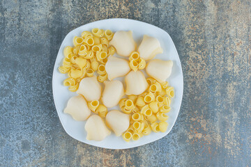 Cooked and uncooked pastas in the bowl, on the marble background