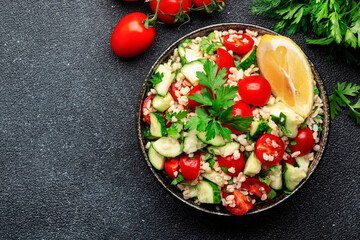 Bulgur tabbouleh salad with fresh tomatoes, cucumbers, parsley and lemon dressing. Traditional Middle Eastern and Arabic dish. Bllack stone kitchen table background, top view