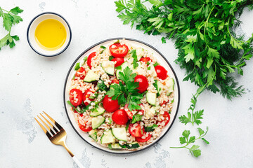 Bulgur tabbouleh salad with fresh tomatoes, cucumbers and parsley. Traditional Middle Eastern and Arabic dish. White kitchen table background, top view
