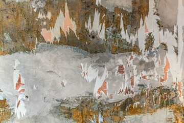 Part of a wall with pieces of torn wallpaper on plaster. Texture of an old dilapidated facade with layers of yellow and white paint