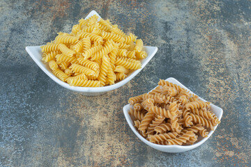 Brown and yellow fusilli pasta in bowl, on the marble background