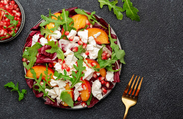 Fresh salad with arugula, radicchio, peaches, feta cheese and pomegranate seeds. Black table...