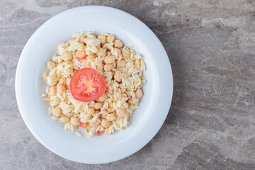 Chickpeas and pasta with slice tomato on the plate , on the marble background