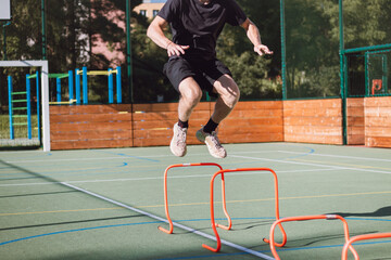 Blond boy in sportswear jumps over red obstacles to improve lower body dynamics. Plyometric training in an outdoor environment. Improve your skills