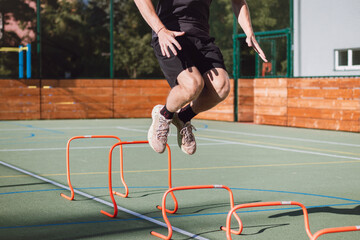 Blond boy in sportswear jumps over red obstacles to improve lower body dynamics. Plyometric training in an outdoor environment. Improve your skills