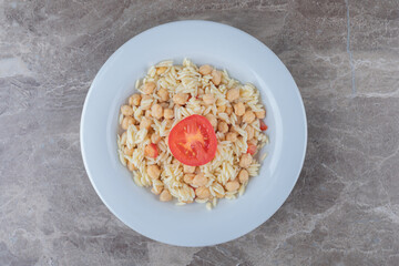 Chickpeas and pasta with slice tomato on the plate , on the marble background