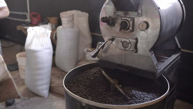 Dark roasted coffee grains being mixed inside of a roaster machine cooling tray