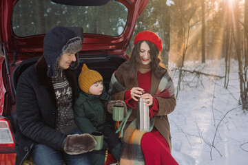 Happy family drinking tea after a walk and sledding in a snowy forest.  Holiday atmosphere. Winter family activities.