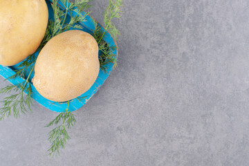 A blue wooden board of uncooked potatoes with fresh dill
