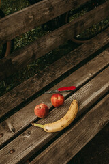 Two peaches and a banana forming a smile on a wooden bench, with a pocket knife.