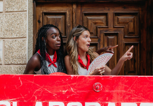 front view of two friends of different ethnicity watching a running of the bulls in a village in spain. They are behind a wooden protection that says "collaborators". concept of diversity, tolerance