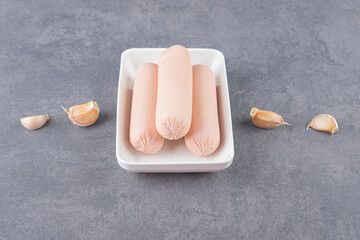 A white plate of boiled sausages with garlics