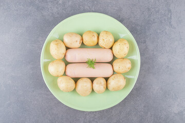 A green plate with boiled sausages and boiled potatoes