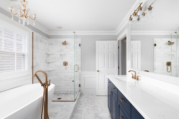 A beautiful bathroom with a blue vanity cabinet, standalone bathtub and shower, and gold faucets. - Powered by Adobe
