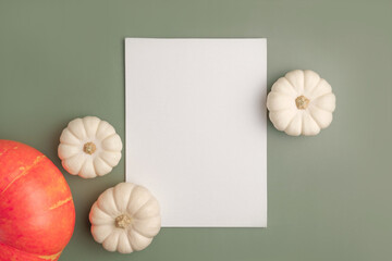 Blank paper sheet with Halloween decorations on pastel green background. Greeting card, invitation mockup. Place for inscription. Pumpkin. Modern Minimal business mock up, template. Flat lay, top view