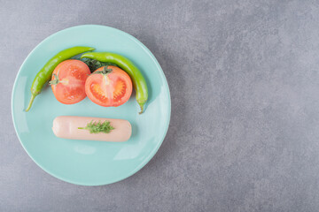 A plate with boiled sausage and sliced red tomato